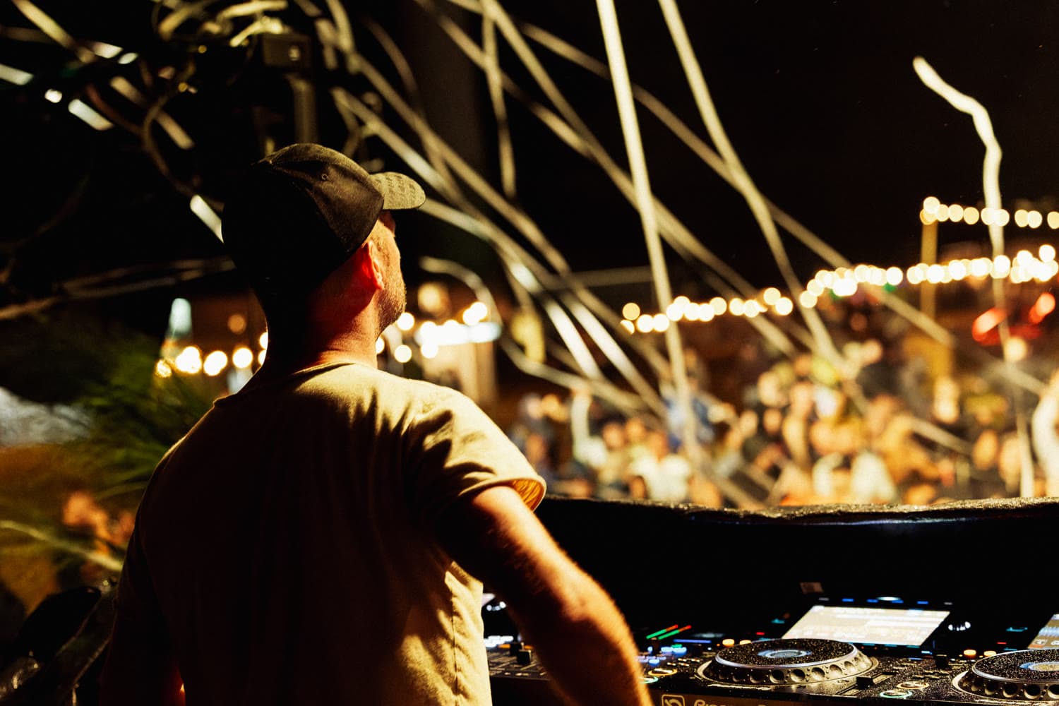 DJ von hinten an den Decks, vor ihm die Menge unter Lichterketten